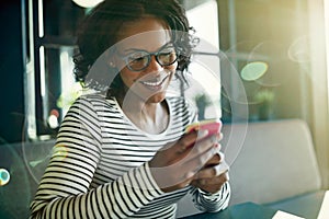 Smiling young African woman sending texts on her cellphone