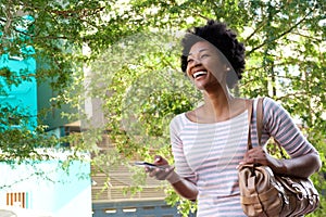 Smiling young african woman walking with mobile phone and purse