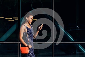 Smiling young african woman walking with phone and earphones