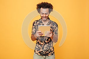 Smiling young afro american guy standing and using pc tablet