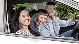 Smiling young arab man and woman with child are driving in car and looking at camera from open window