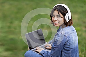 Smiling Young Arab Woman In Headphones Using Laptop With Blank Screen Outdoors