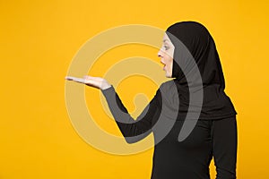 Smiling young arabian muslim woman in hijab black clothes showing pointing copy space with hands finger isolated on