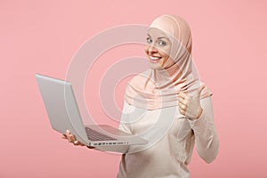 Smiling young arabian muslim woman in hijab light clothes posing isolated on pink background. People religious lifestyle