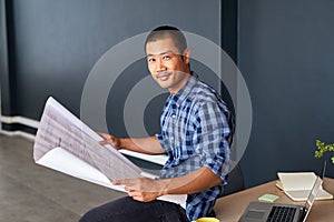 Smiling young Asian architect reading blueprints in an office