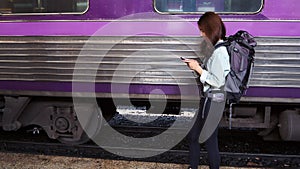 Smiling young Asian backpacker walking and using mobile smart phone on train station. Internet of thing concept.