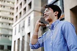 Smiling Young Asian Businessman Using Mobile Phone in Big Urban City