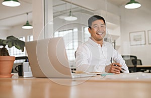 Smiling young Asian businessman working alone at his office desk