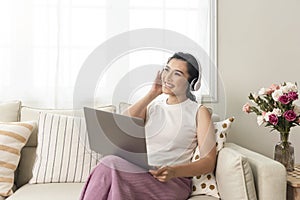 Smiling young asian businesswoman using laptop computer while relaxing on a couch at home. work from home concept