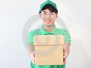 Smiling young Asian delivery man in green T-shirt uniform and cap holding cardboard box on white background, giving box on camera