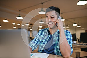 Smiling Asian designer talking on a cellphone in an office