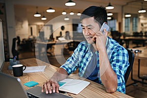 Smiling Asian designer talking on a cellphone and working online