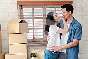 Smiling young Asian happy couple hugging boyfriend with cardboard boxes at moving day in their new home after buying real estate.