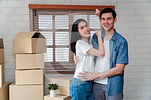 Smiling young Asian happy couple hugging boyfriend with cardboard boxes at moving day in their new home after buying real estate.