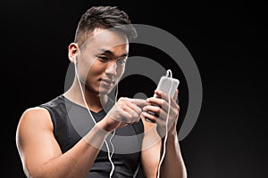 smiling young asian man in earphones using smartphone