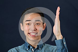 Smiling young Asian man holding his hand upright