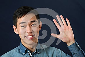 Smiling young Asian man waving his palm