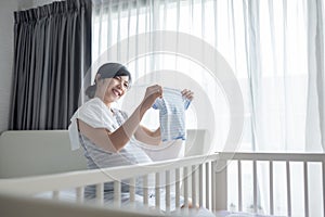 Smiling Young Asian Pregnant Female looking at baby clothes while packing her clothing and getting ready for maternity hospital