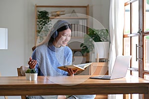 Smiling young asian teen girl wear headphones video calling on laptop. Happy pretty woman student looking at computer screen