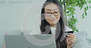 Smiling young Asian woman cheering after successfully making online payment using credit card from laptop at home