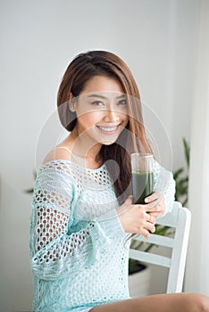 Smiling young asian woman drinking green fresh vegetable juice o