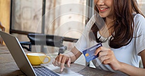 The smiling young Asian woman enjoys shopping online via a smartphone and paying online via credit card. Convenience of spending w