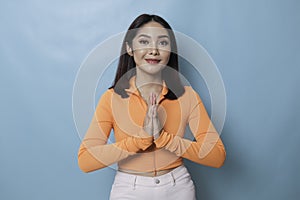 Smiling young Asian woman gesturing greeting or namaste isolated over white background