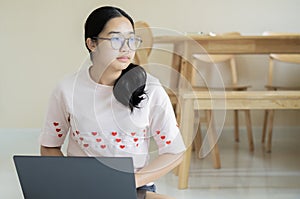 Smiling young Asian woman in glasses sit on floor and working on laptop or studying online at home