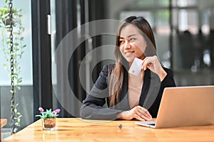 Smiling young asian woman holding credit card and using laptop computer for banking or shopping online