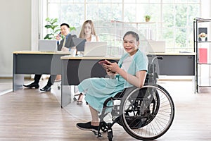 Smiling young Asian woman office worker in wheelchair holding tablet look at camera, disabled people working with colleague