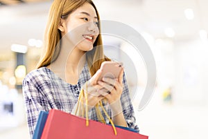 Smiling young Asian woman with shopping colour bags over mall background. using a smart phone shopping online  and smiling while