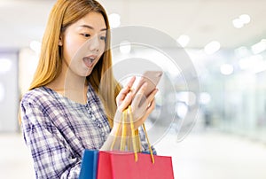 Smiling young Asian woman with shopping colour bags over mall background. using a smart phone shopping online  and smiling while