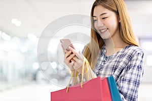 Smiling young Asian woman with shopping colour bags over mall background. using a smart phone shopping online  and smiling while