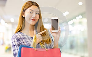 Smiling young Asian woman with shopping colour bags over mall background. using a smart phone shopping online  and smiling while