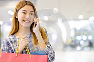 Smiling young Asian woman with shopping colour bags over mall background. using a smart phone shopping online  and smiling while