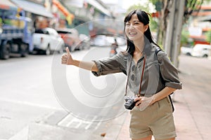 Smiling young Asian woman traveler hitchhiking on a road in the city. Life is a journey concept