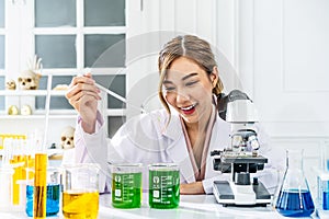 Smiling young asian woman wearing scientist uniform working at scientist laboratory with measuring liquid at laboratory