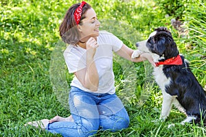 Smiling young attractive woman playing with cute puppy dog border collie in summer garden or city park outdoor