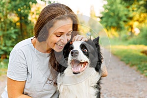 Smiling young attractive woman playing with cute puppy dog border collie on summer outdoor background. Girl holding