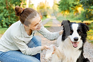 Smiling young attractive woman playing with cute puppy dog border collie on summer outdoor background. Girl holding