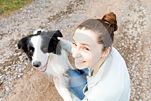 Smiling young attractive woman playing with cute puppy dog border collie on summer outdoor background. Girl holding