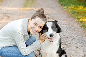 Smiling young attractive woman playing with cute puppy dog border collie on summer outdoor background. Girl holding