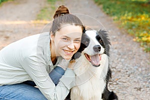 Smiling young attractive woman playing with cute puppy dog border collie on summer outdoor background. Girl holding