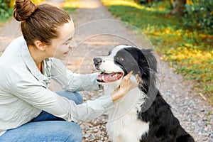 Smiling young attractive woman playing with cute puppy dog border collie on summer outdoor background. Girl holding