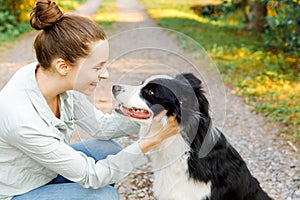 Smiling young attractive woman playing with cute puppy dog border collie on summer outdoor background. Girl holding
