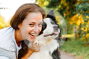 Smiling young attractive woman playing with cute puppy dog border collie on summer outdoor background. Girl holding