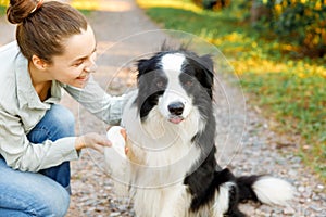 Smiling young attractive woman playing with cute puppy dog border collie on summer outdoor background. Girl holding