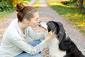 Smiling young attractive woman playing with cute puppy dog border collie on summer outdoor background. Girl holding