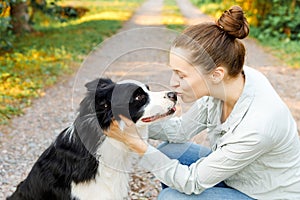 Smiling young attractive woman playing with cute puppy dog border collie on summer outdoor background. Girl holding