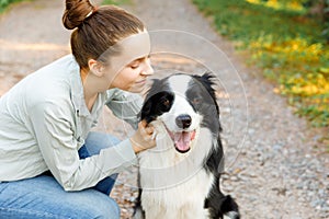 Smiling young attractive woman playing with cute puppy dog border collie on summer outdoor background. Girl holding